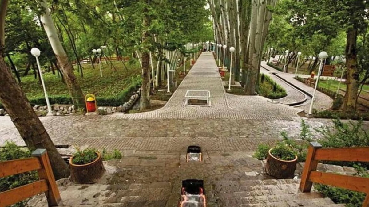 Serene view of Vakilabad Park in Mashhad, Iran, featuring a peaceful waterway surrounded by manicured greenery, wooden fences, and lush trees, providing a tranquil escape in nature.
