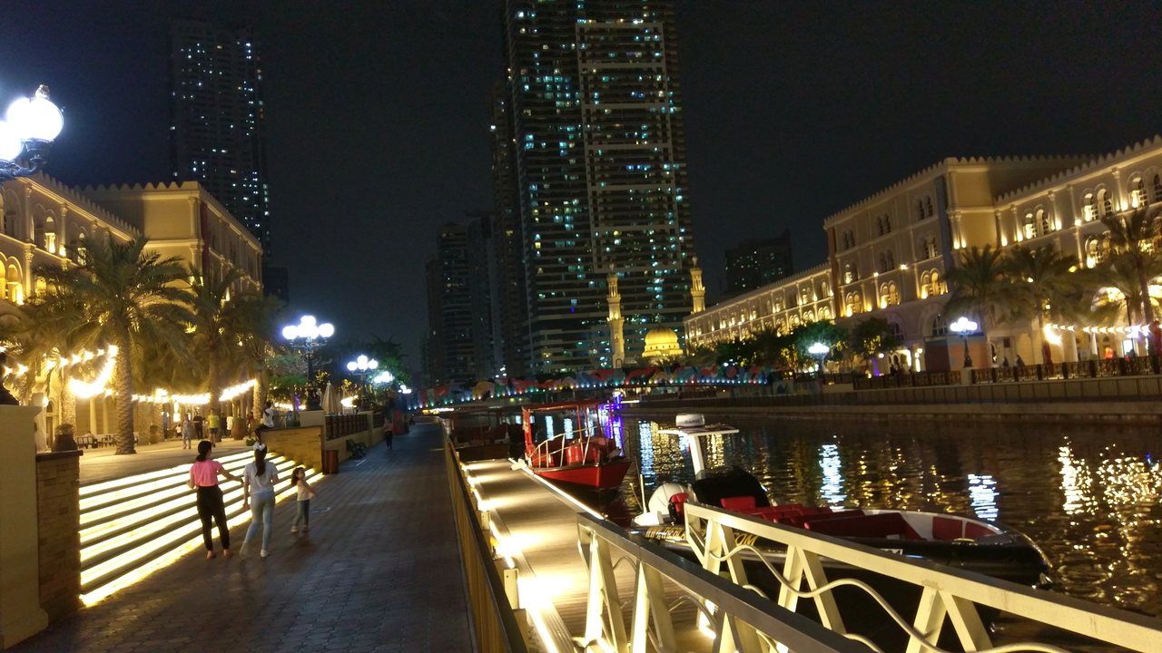 Al Qasba Canal at night with illuminated waterfront promenade and boats in Sharjah, UAE