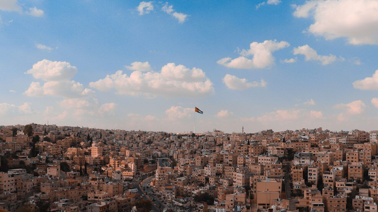 Panoramic view of Amman’s hillside cityscape with the Jordanian flag under a blue sky