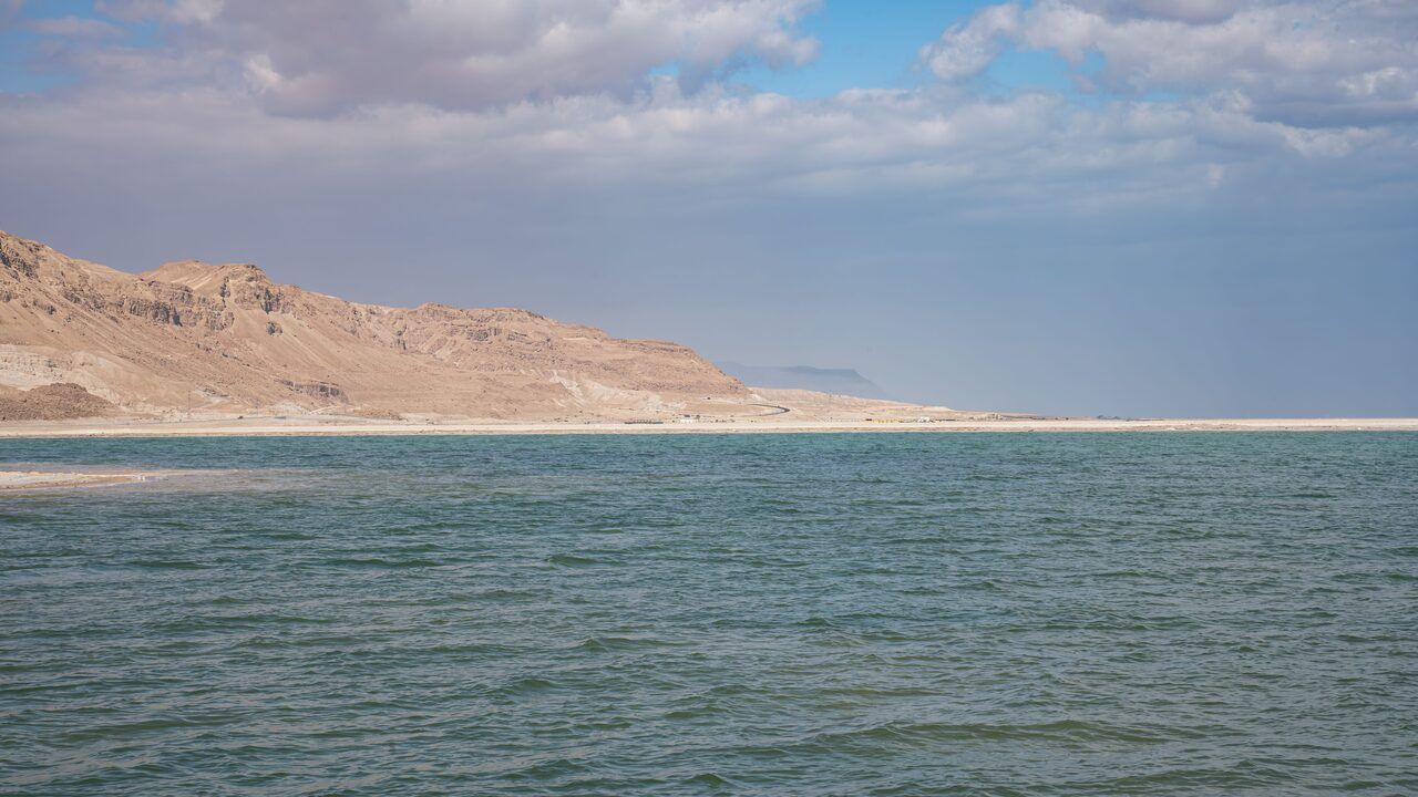 Wide view of the Dead Sea with blue water and desert mountains along the Jordanian shore