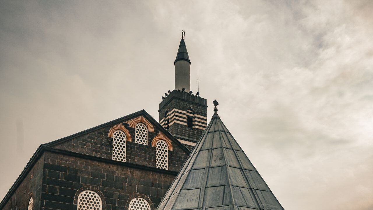 Wide view of Diyarbakir Grand Mosque featuring its historic basalt facade, minaret and conical courtyard roof.