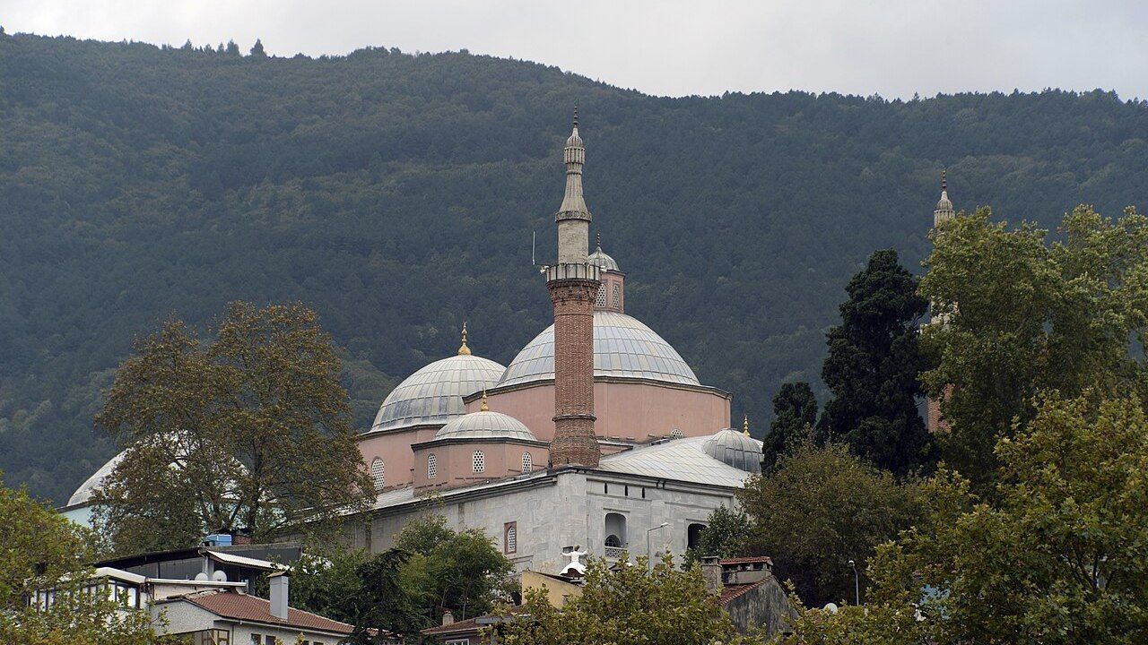 Wide view of the Green Mosque and Green Tomb complex in Bursa with forested mountains in the background