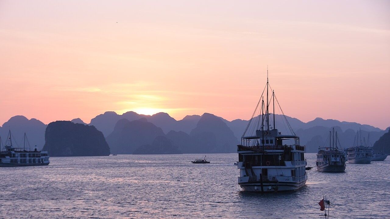Cruise boats sailing among limestone islands in Ha Long Bay Vietnam at sunset
