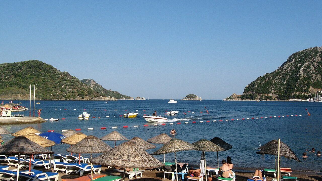 Panoramic view of Icmeler Beach with colorful umbrellas and forested hills.