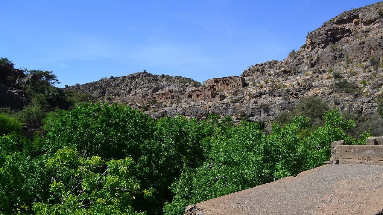 Wide scenic view of a mountain village surrounded by lush greenery and rocky slopes in Jabal Akhdar, Oman.