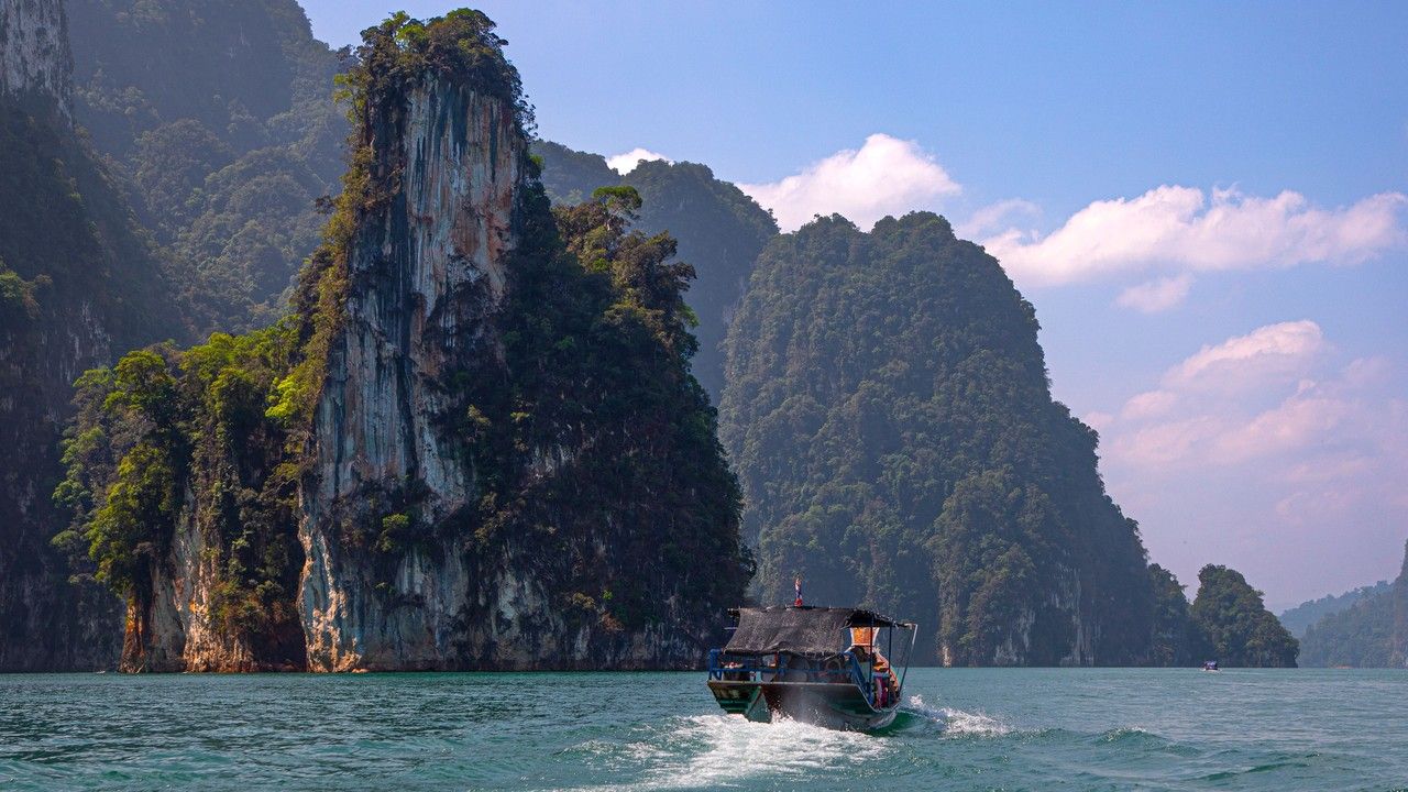 Long-tail boat on Cheow Lan Lake surrounded by limestone cliffs in Khao Sok National Park, Thailand