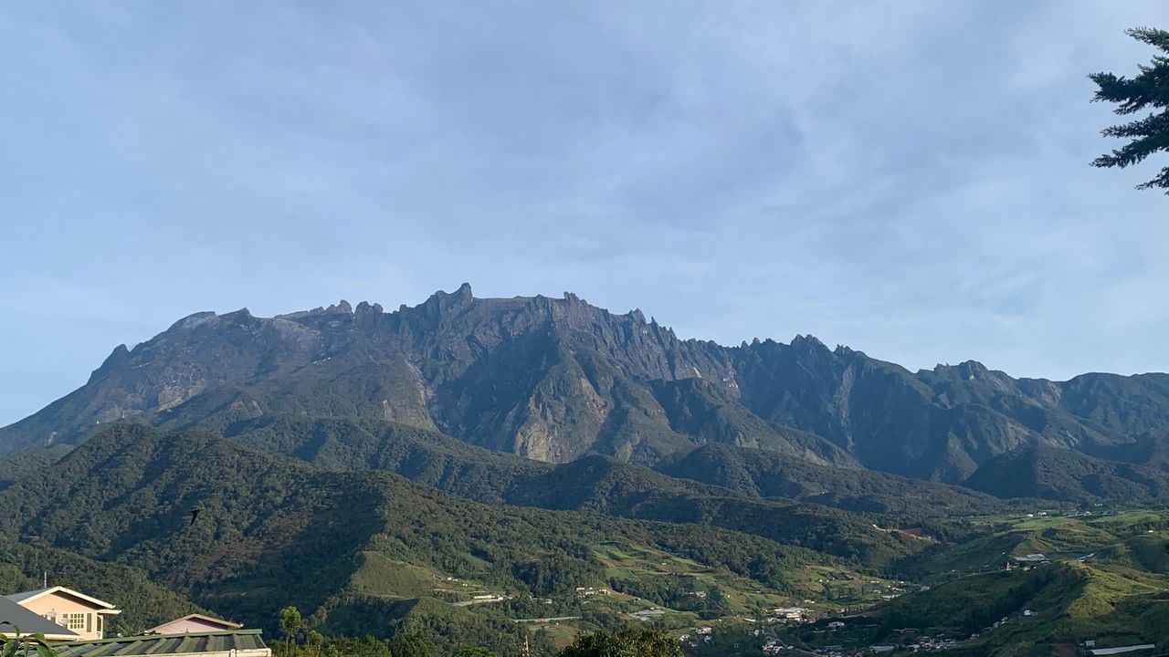 Wide scenic view of Mount Kinabalu rising above the lush green hills and valleys of Kundasang, Sabah, Malaysia.