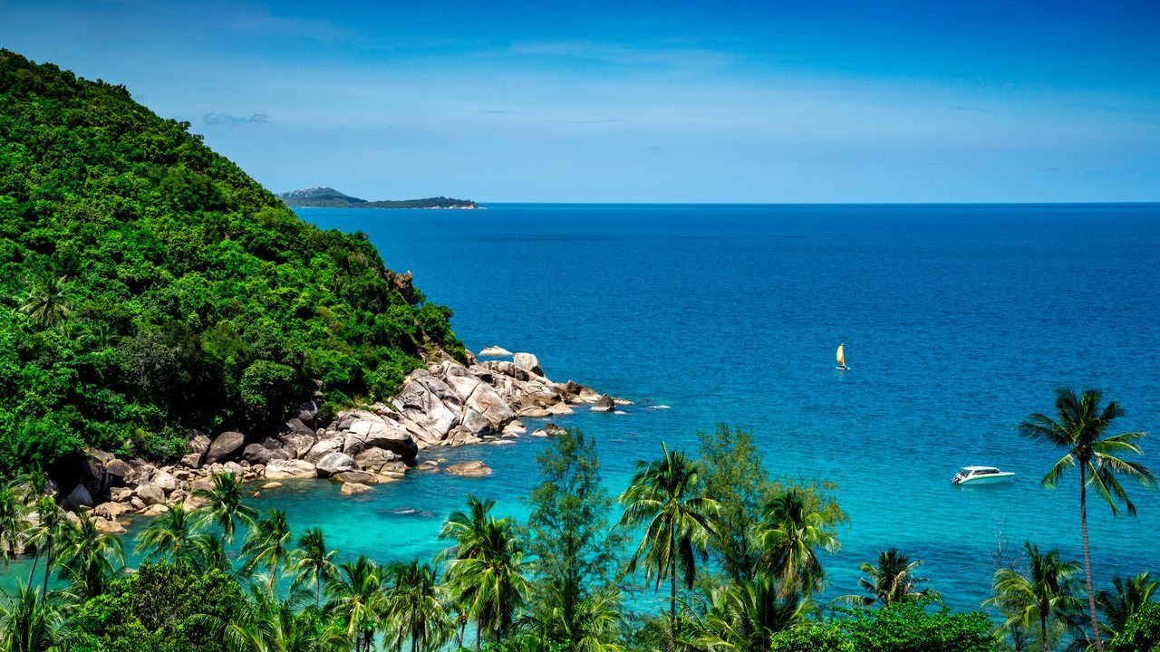 Wide tropical coastline view with turquoise sea, palm trees and lush greenery in Koh Samui, Thailand
