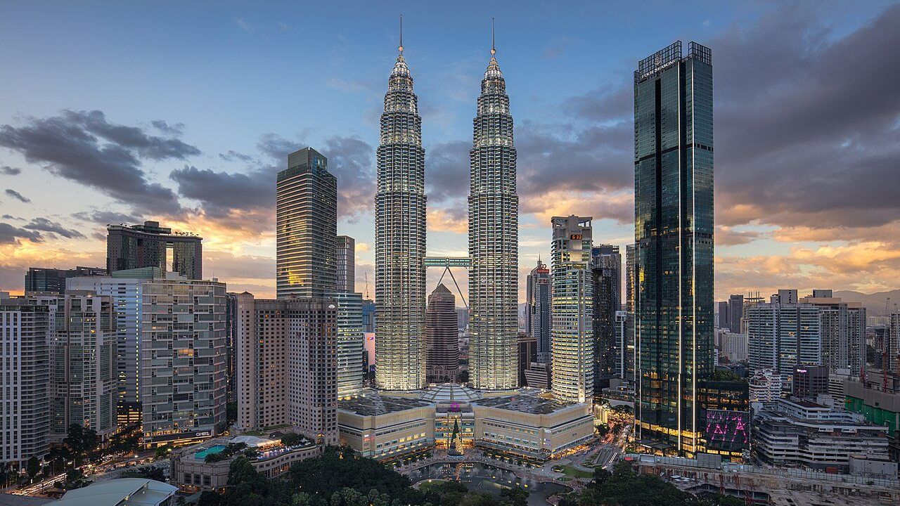 Wide view of the Petronas Twin Towers and Kuala Lumpur skyline at sunset in Malaysia.
