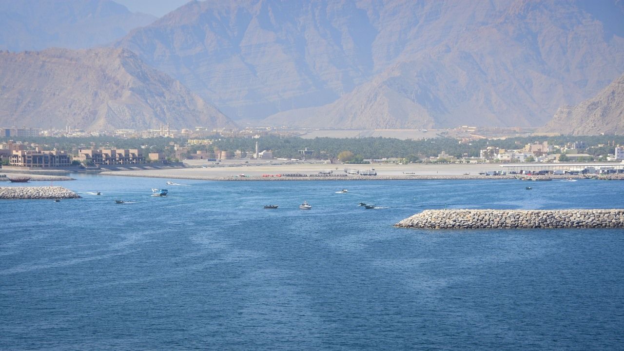 Wide scenic view of Khasab harbor with blue sea, boats and the dramatic Musandam Mountains in Oman.