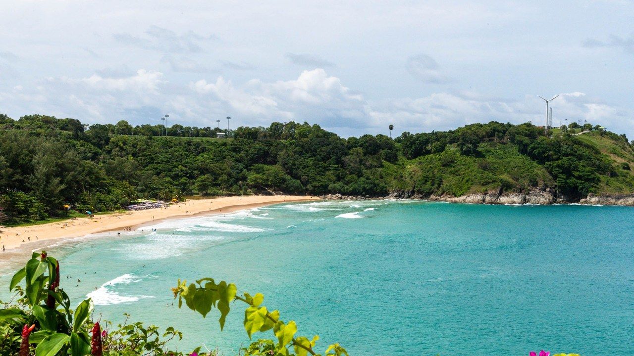 Wide view of a tropical beach with turquoise water and green hills in Phuket, Thailand