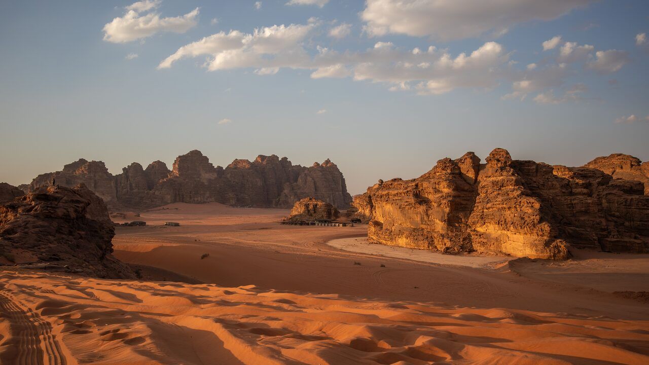 Wide panoramic view of Wadi Rum’s red sand dunes and sandstone mountains at golden hour in Jordan
