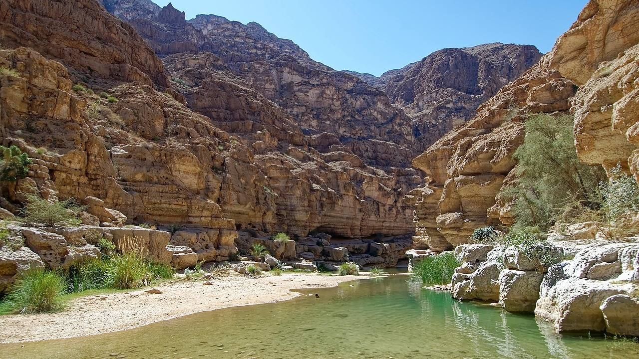 Wide scenic view of Wadi Shab with clear water flowing between dramatic rocky canyon walls in Oman.